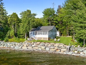 A house with a porch, a stone wall, and a grassy yard.