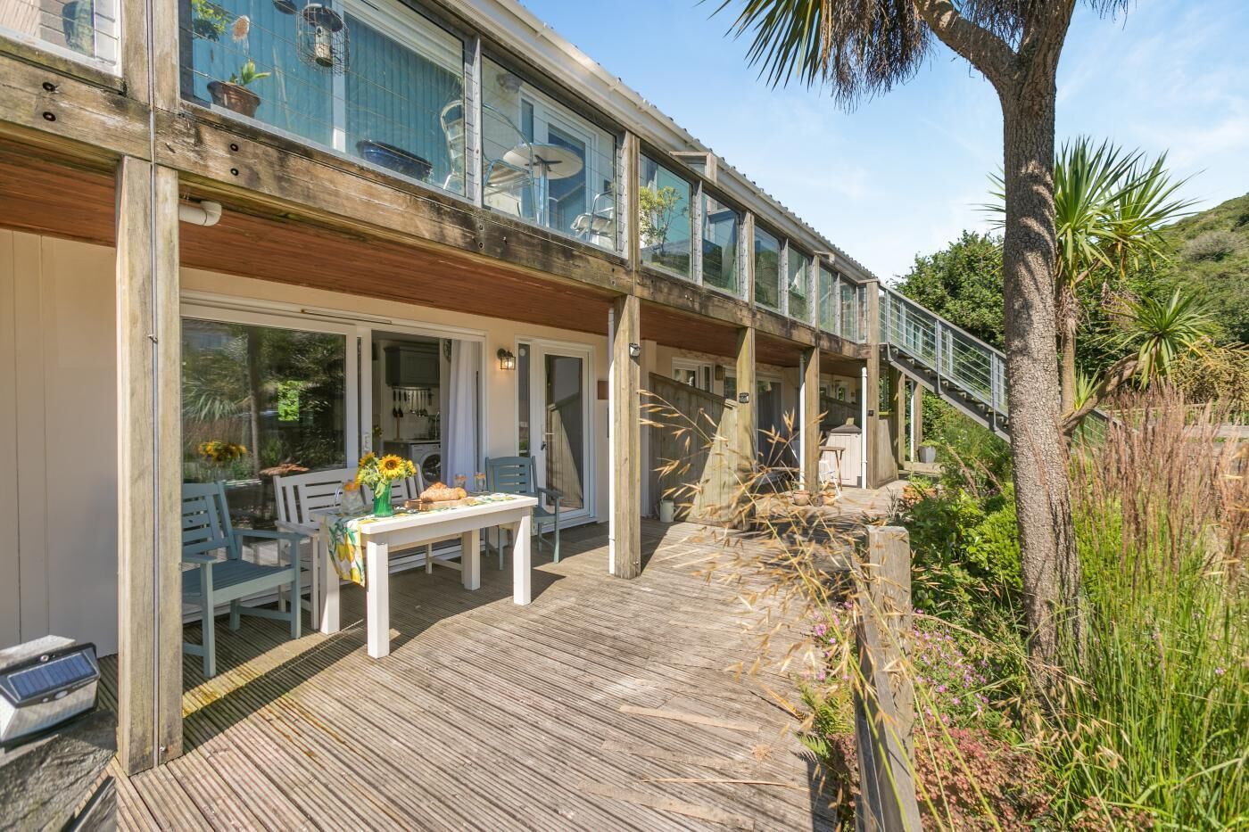 A wooden deck with a table and chairs, a glass-enclosed balcony, and a view of the surrounding landscape.