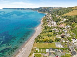 Vista aérea de uma vila costeira com praia, casas e vegetação.