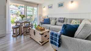 Un salon chaleureux avec un canapé gris, une table basse en bois et un coin repas avec une table dressée pour deux personnes.