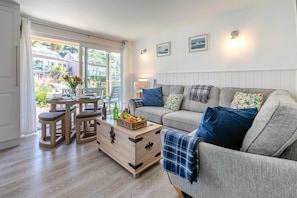 A cozy living room with a grey sofa, wooden coffee table, and a dining area with a table set for two. - 2 Bed in Torpoint (oc-88478) (Downderry)