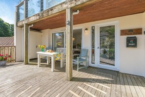 Um deck de madeira com mesa e cadeiras, uma porta de vidro que dá para um jardim, e uma placa com a inscrição 'POST'.