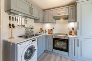 A compact kitchen with a built-in washer, oven, and a variety of utensils on the wall. - 2 Bed in Torpoint (oc-88478) (Downderry)