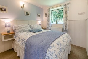 Quarto com cama, mesas de cabeceira, luzes na parede, janela com cortinas e radiador.