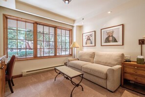 Ein Zimmer mit großem Fenster, einer Couch, einem kleinen Tisch, einer Lampe und zwei gerahmten Bildern an der Wand.