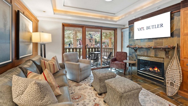 Una sala de estar con chimenea, un sofá, un sillón y una televisi ón mostrando 'VAIL BUTLER'.