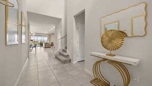 Un couloir avec un escalier, une console ornée d’un objet décoratif doré et un grand miroir avec un cadre doré.