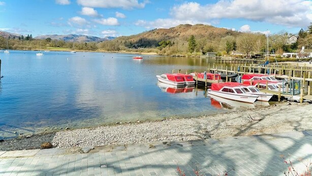 Un lago tranquilo con barcos amarrados a un muelle de madera, rodeado de colinas y árboles dispersos.