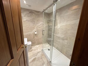 Une salle de bain moderne avec une douche à parois de verre, des murs en marbre et une porte en bois.