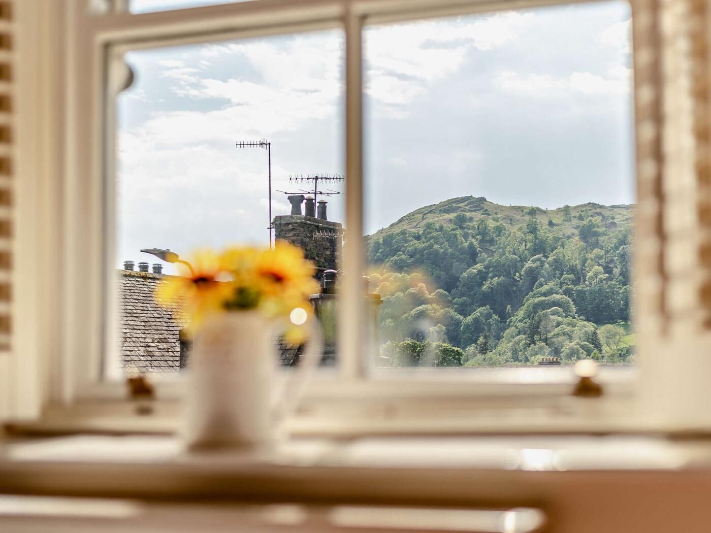 A window with a view of a green hill and a building with antennas.