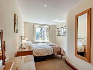 Une chambre à coucher avec un lit, une table de chevet, une lampe, une fenêtre et un grand miroir.