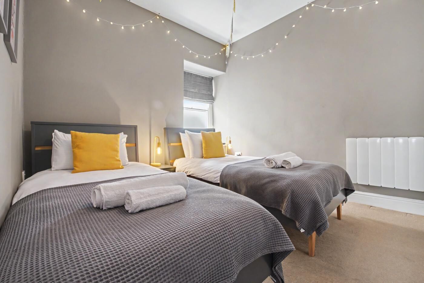 Ein Hotelzimmer mit zwei Betten, einem Fenster, einer Heizung und Lichterketten.