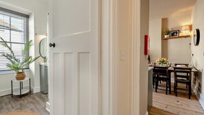 Ein Flur, der in einen Essbereich führt, mit einem für vier Personen gedecktem Tisch, einer Zimmerpflanze und einem Spiegel an der Wand.