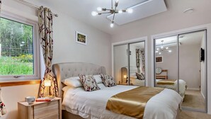 Ein Schlafzimmer mit einem großen Bett, Nachttischen, einer Lampe, einem Fenster mit Vorhängen, einer Deckenleuchte und einem Spiegel.