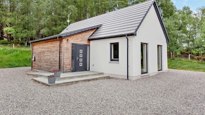 Ein modernes, zweistöckiges Haus mit geneigtem Dach, einem Holzanbau und einer Einfahrt mit Kies.