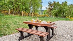 Ein Picknicktisch mit Bänken und einer Auswahl an Speisen und Getränken auf einem Kiesweg, umgeben von viel Grün.