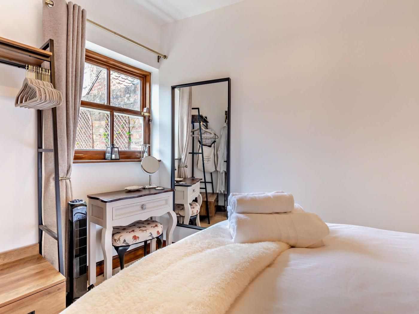 Ein Schlafzimmer mit einem Bett, einem Schminktisch, einem Spiegel und einem Fenster mit Vorhängen.