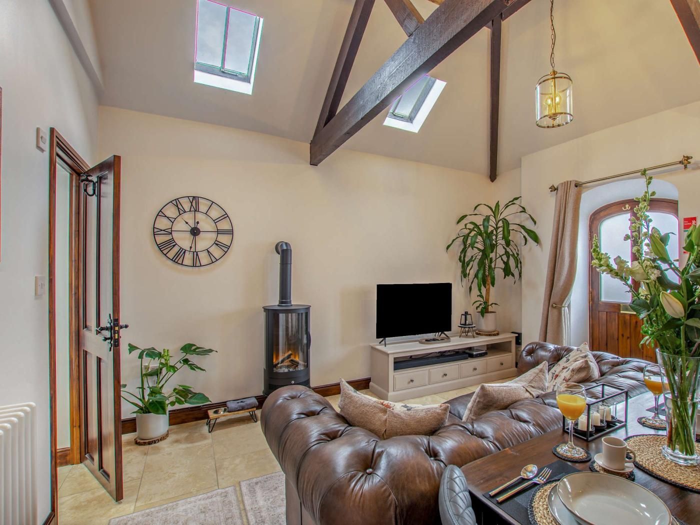A living room with a fireplace, leather sofa, television, and a clock on the wall.
