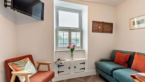 A living room with a sofa, a chair, a small table, a window with blinds, a flat-screen TV mounted on the wall, and a decorative wall piece. - 2 Bed in Frizington (oc-95126) (Arlecdon)