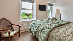 A bedroom with a bed, a chair, two windows with curtains, a flat-screen TV, and a mirror. - 2 Bed in Frizington (oc-95126) (Arlecdon)