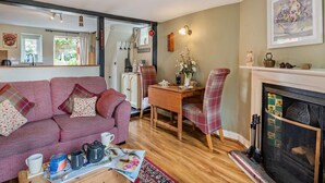 Un salon chaleureux avec un canapé, une table à manger, une cheminée et un coin cuisine visible à travers une porte ouverte.