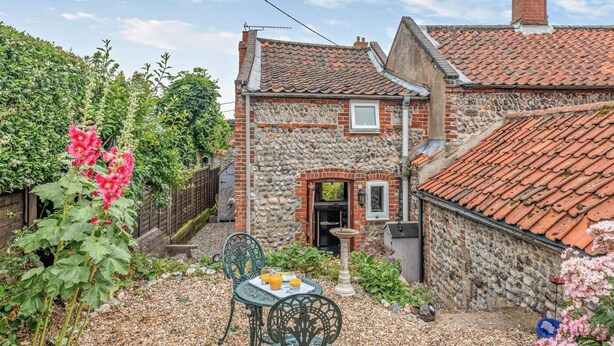 Une maison en pierre avec un toit de tuiles, un jardin fleuri et une table avec des boissons.