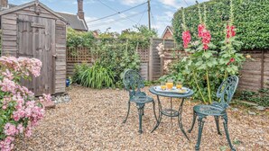 Une terrasse de jardin avec une table et des chaises, entourée d’une clôture en bois et d’un abri de jardin.