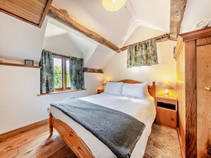 Ein Schlafzimmer mit einem hölzernen Bett, einem Nachttisch, einer Lampe und einem Fenster mit Vorhängen.