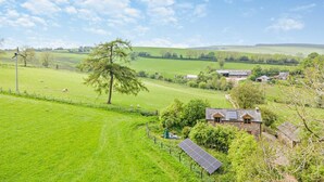 Ländliche Landschaft mit einem Steinhaus, einer Windkraftanlage und einer Solaranlage.