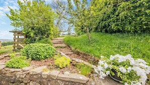 Ein Gartenpfad mit Steinmauern, einer Holzpergola und verschiedenen Pflanzen.