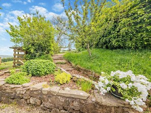 A garden pathway with stone walls, a wooden pergola, and various plants.