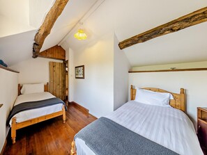 A bedroom with two wooden beds, a wooden ceiling beam, and a framed picture on the wall.