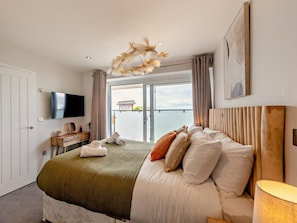 Ein Hotelzimmer mit Bett, Fernseher, Schreibtisch mit Stuhl, Fenster mit Aussicht und einer Deckenleuchte.