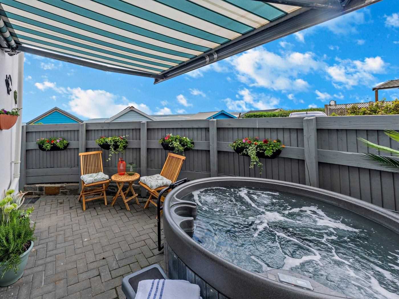 Eine Terrasse mit Whirlpool, zwei Holzstühlen, einem Tisch und einem überdachten Bereich mit gestreifter Markise.