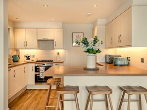 Eine moderne Küche mit Holzausstattung, einer zentralen Kochinsel mit Barhocker, einem Gasherd und einem Toaster.