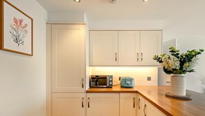 Een moderne keuken met witte kasten, een houten aanrecht, een magnetron, een broodrooster en een vaas met bloemen.