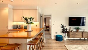 Een moderne keuken met een houten kookeiland, barkrukken, een televisie, en een zithoek met een bank en planten.