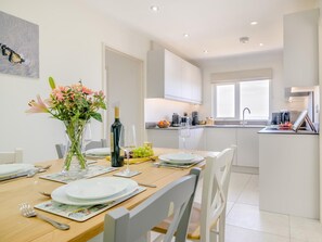 Une cuisine moderne avec des meubles blancs, une table à manger dressée avec des assiettes, des verres et un vase de fleurs.