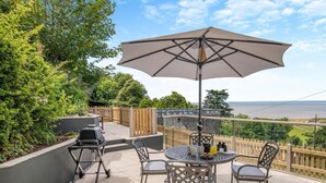 Una terrazza esterna con un tavolo rotondo, quattro sedie, un barbecue e un ombrellone grande.