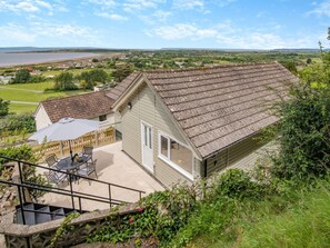 Une maison avec un toit en pente, une terrasse dotée de mobilier d’extérieur et une vue sur un lac et les environs.