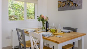 Un'area pranzo con un tavolo apparecchiato per quattro persone, una finestra vista sul verde e un quadro appeso al muro.