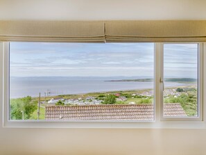 Une pièce dotée d’une grande fenêtre donnant sur un paysage côtier, avec une plage et des maisons.