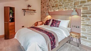 Ein Schlafzimmer mit Steinwand, einem Holzschrank, einem Bett mit weißer Bettwäsche, einem Nachttisch mit Lampe und einem kleinen Holztisch.