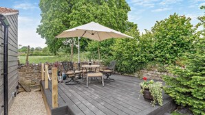 Eine Holzterrasse mit Gartenmöbeln, einer Pergola und einer Steinmauer.