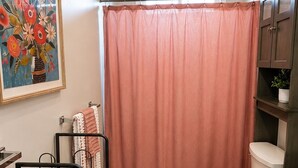 Un baño con cortina de ducha, inodoro, lavamanos y un estante con una planta.