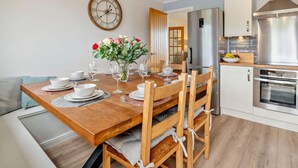 Une cuisine moderne avec une table à manger en bois pour quatre personnes, un réfrigérateur en acier inoxydable et un four encastré.