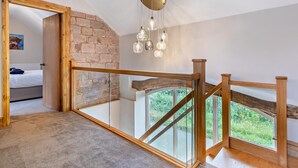 Une pièce avec un mur en pierre, un escalier en bois et une vue sur la verdure à l’extérieur.