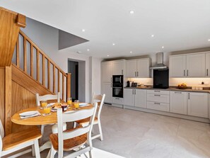 A modern kitchen with white cabinets, a wooden staircase, and a dining area with a table set for two. - 2 Bed in Stoke-on-trent (oc-95164) (Longsdon)