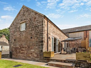 A stone building with a sloped roof, a patio area with outdoor seating, and a wooden fence. - 2 Bed in Stoke-on-trent (oc-95164) (Longsdon)