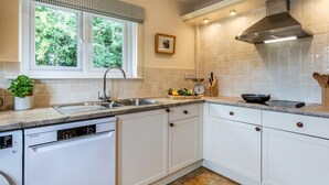 Een keuken met witte kastjes, een vaatwasser, een raam met geruit gordijn en een roestvrijstalen afzuigkap.